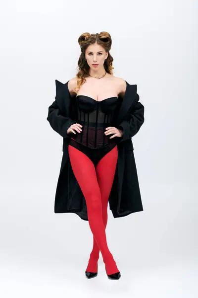 Confident young woman in trendy red tights and a chic black coat poses in a minimal setting. — Stock Photo