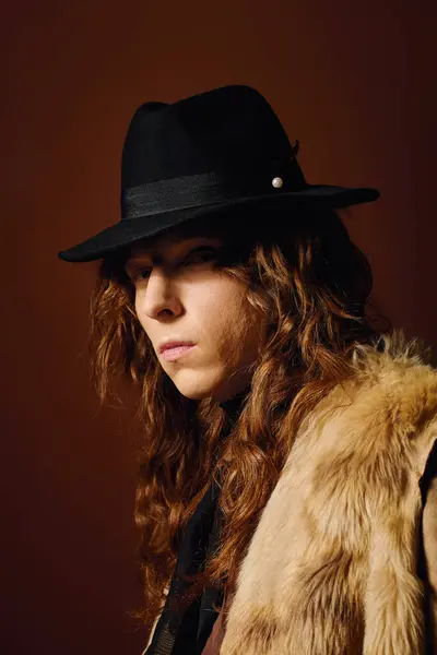 A young man poses confidently, showcasing his stylish hat and flowing hair against a rich backdrop. — Stock Photo