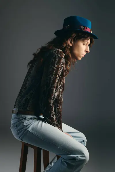 A handsome young man quietly reflects while sitting on a stool, wearing a fashionable hat. — Stock Photo