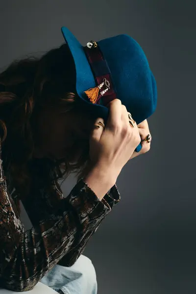 Un bel giovane uomo con i capelli ricci indossa un sorprendente cappello blu mentre si perde nella contemplazione. — Foto stock