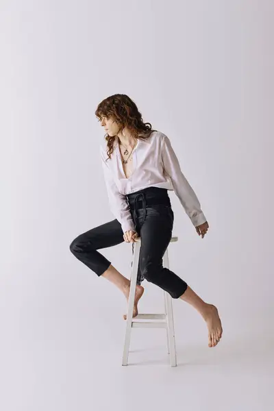 A handsome young man confidently poses in stylish outfits on a white stool. — Stock Photo