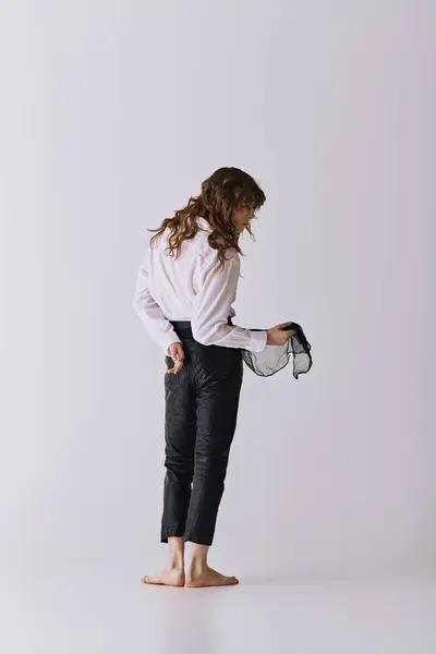 A young man stands barefoot, holding a delicate accessory while reflecting on his look. — Stock Photo