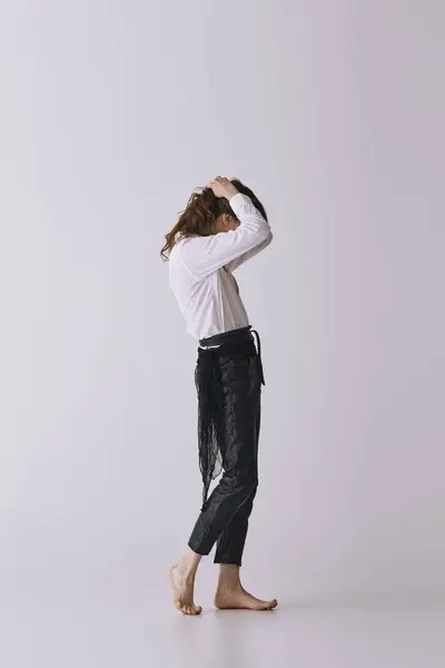A handsome young man stands barefoot, running his hands through his hair, exuding effortless style. — Stock Photo