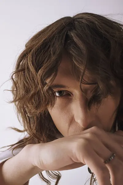Young man with curly hair seated, gazing intently with a thoughtful expression, showcasing style. — Stock Photo