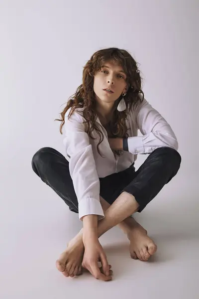 A handsome man with long hair sits elegantly on the floor, showcasing his fashionable style. — Stock Photo