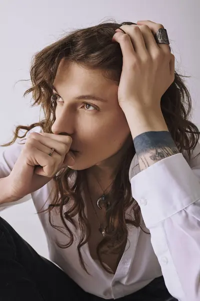 Handsome young man with long hair looks contemplative while seated in a minimalistic room. — Stock Photo