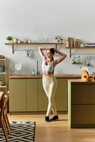 A young woman dances in a bright kitchen, wearing leggings and a sports bra. — Stock Photo