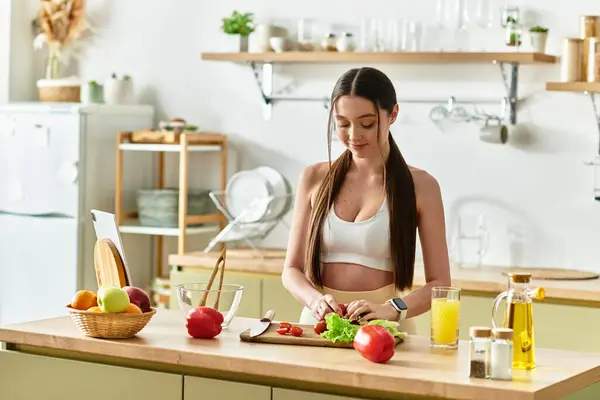 En una cocina elegante, una mujer joven en forma hábilmente corta verduras frescas para una ensalada saludable. - foto de stock