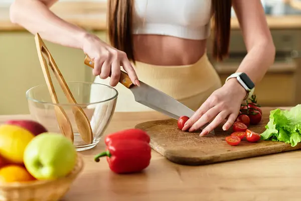 Tiro cortado de jovem mulher em um sutiã esportivo prepara uma salada vibrante em sua cozinha usando legumes frescos. — Fotografia de Stock