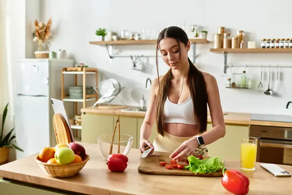 A fit young woman joyfully cooks in the modern kitchen, chopping colorful vegetables for a salad. — Stock Photo