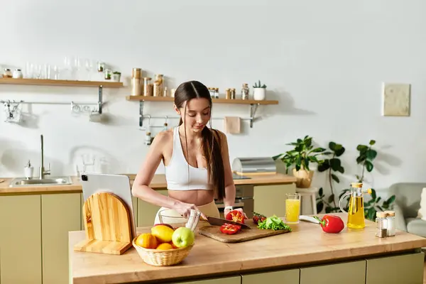 A fit young woman prepares a colorful salad in her modern kitchen, enjoying healthy cooking. — Stock Photo