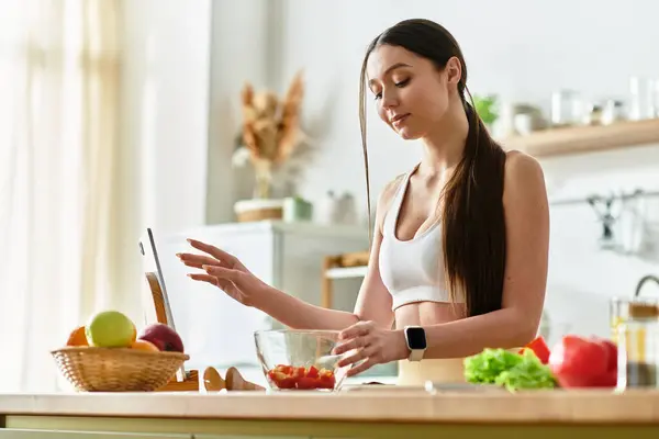 Подтянутая молодая женщина в спортивном лифчике умело готовит вкусный салат на своей солнечной кухне.. — стоковое фото