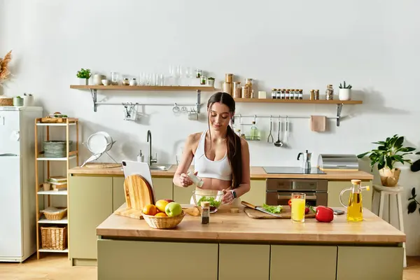 A fit woman in sportswear makes a fresh salad in a stylish kitchen with vibrant ingredients. — Stock Photo