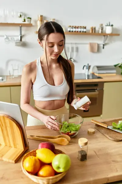 A young woman in sportswear skillfully prepares a vibrant salad in a modern kitchen. — Stock Photo