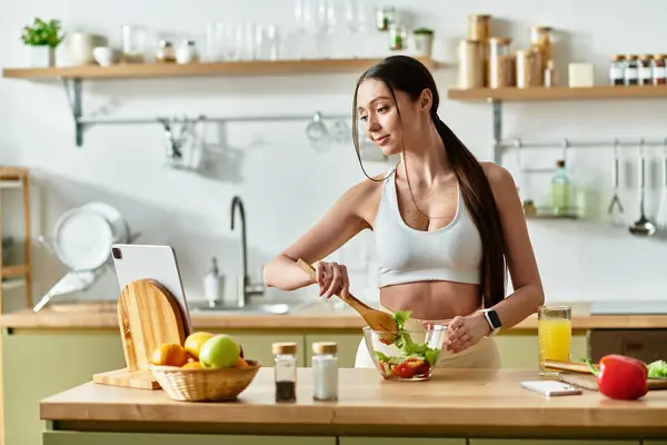 In a bright kitchen, a fit young woman skillfully makes a salad while enjoying cooking. — Stock Photo