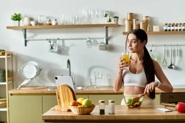 Young woman in sports bra prepares a vibrant salad while enjoying a refreshing drink. — Stock Photo