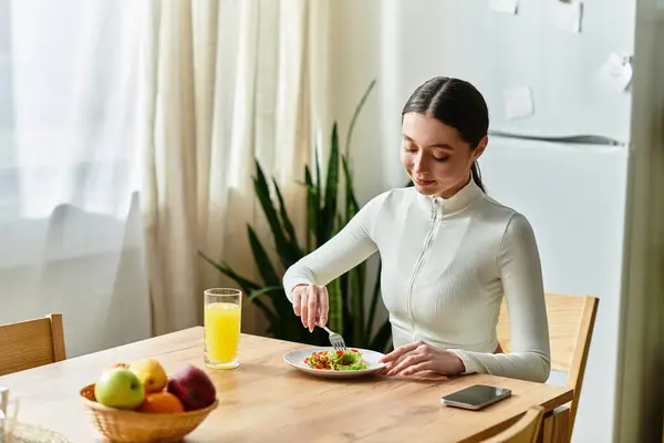 Eine junge Frau sitzt an einem Holztisch und genießt einen bunten Salat mit erfrischendem Saft in der Nähe. — Stockfoto