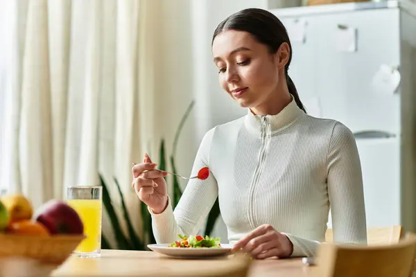 A beautiful young woman savors a nutritious meal at home, enjoying fresh vegetables and juice. — Stock Photo