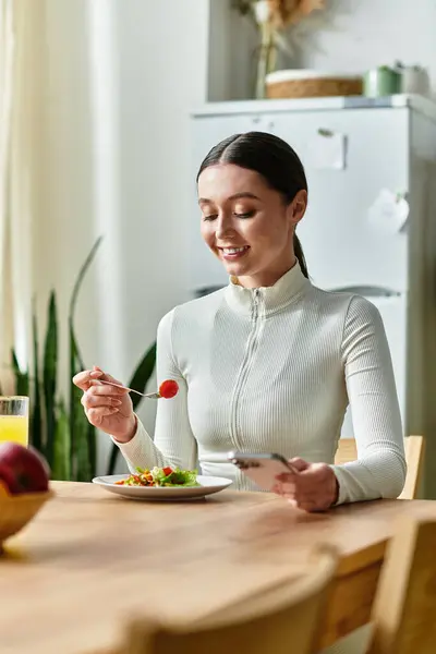 Una bella giovane donna siede a un tavolo di legno, assaporando una colazione sana con un sorriso. — Foto stock