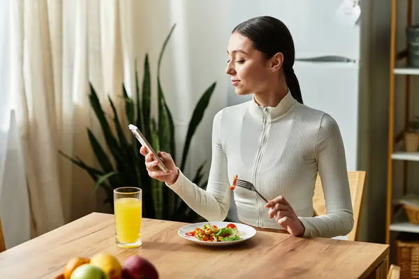 A young woman savors a healthy breakfast while checking her phone in a bright kitchen. — Stock Photo