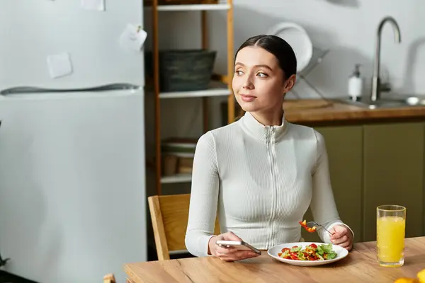 Una mujer joven disfruta de un desayuno saludable con ensalada y jugo en su acogedor espacio de cocina. — Stock Photo