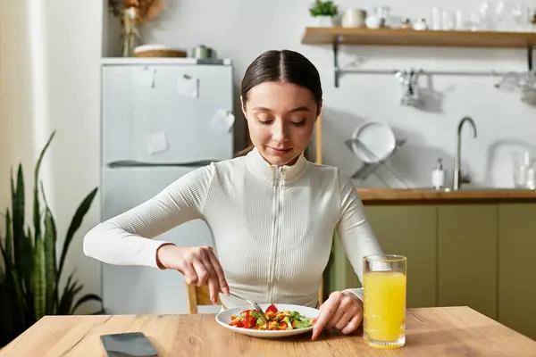Beautiful young woman savoring a nourishing breakfast of salad and juice at home. — Stock Photo