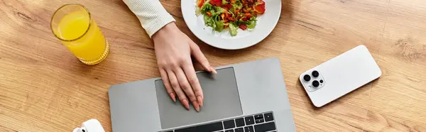 Молодая женщина наслаждается свежим салатом и соком, работая за своим кухонным столом, начиная с ее дня, баннер — стоковое фото