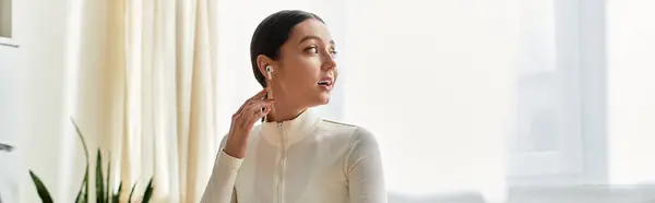 A beautiful young woman sits in her modern kitchen, listening music in earphones, banner — Stock Photo