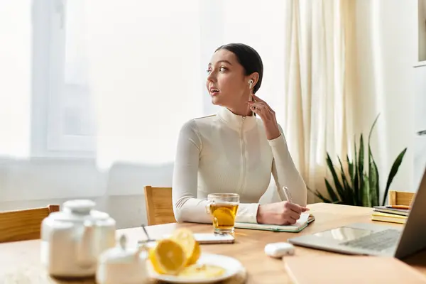 Young woman works on her laptop at home, sipping tea and taking notes, radiating focus. — Stock Photo