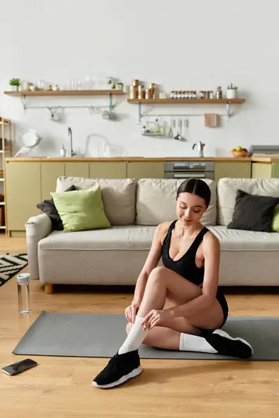 Beautiful young woman in black sportswear stretches on a mat in her modern apartment. — Stock Photo