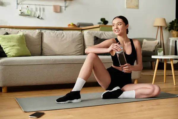 Uma jovem mulher de sportswear preto se estende e sorri em seu apartamento moderno. — Fotografia de Stock
