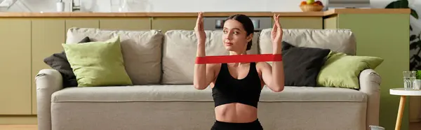 Beautiful young woman exercises with a resistance band in her modern living space, banner — Stock Photo
