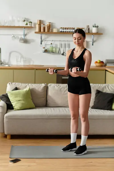 Uma bela jovem mulher em exercícios de sportswear preto com halteres em seu espaço de vida moderno. — Fotografia de Stock