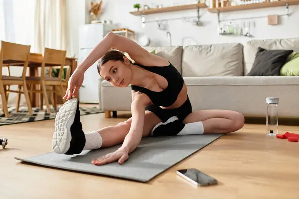 A young woman in black sportswear stretches on a yoga mat in her modern apartment. — Stock Photo