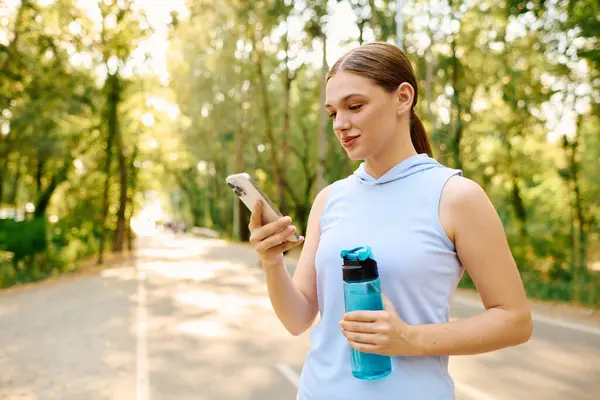 Sporty woman in athletic wear enjoying a sunny day while checking her phone in nature. — Stock Photo