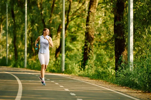 Una giovane donna atletica si esibisce con grazia su una pista liscia fiancheggiata da alberi vivaci e luce solare. — Foto stock