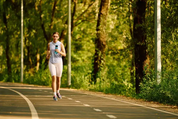 Young athletic woman runs confidently along a tree lined pathway on a bright morning. — Stock Photo