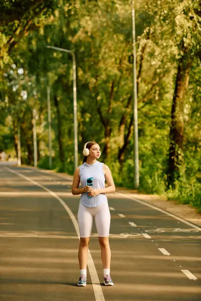 A sporty woman stands confidently with a drink, enjoying nature on a sunny day. — Stock Photo