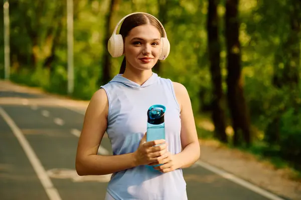 Sporty female jogger embraces nature during a refreshing run, staying hydrated and motivated. — Stock Photo
