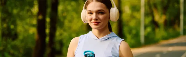 A young woman in headphones smiles while taking a break during her jog in a sunny park. — Stock Photo
