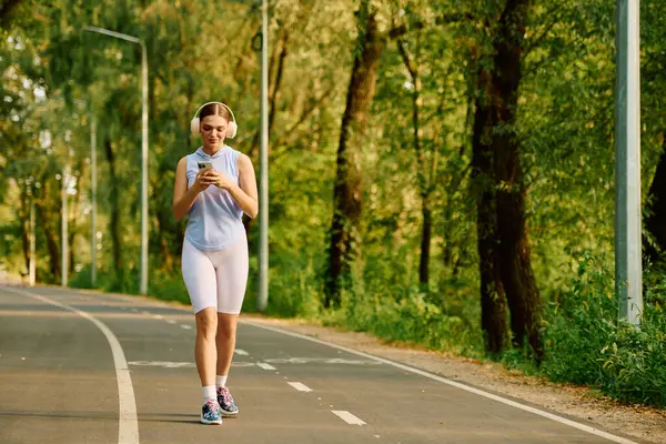 Young beautiful woman in athletic wear strolls along a tree lined path enjoying her music. — Stock Photo