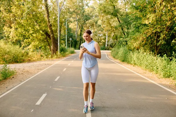 Young athletic woman takes a break on a forested trail, checking her phone with a smile. — Stock Photo