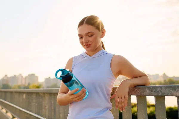 A vibrant young woman relaxes with a water bottle, enjoying the sun and urban view post workout. — Stock Photo