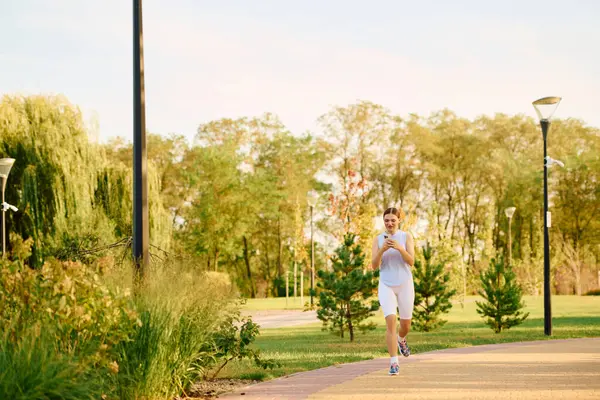 A young beautiful sporty woman jogs through a lively park filled with greenery under a bright sky. — Stock Photo