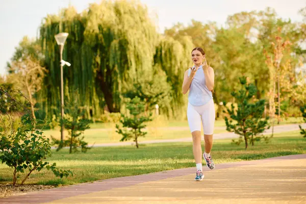 Sporty woman enjoys jogging along a beautiful pathway surrounded by lush greenery. — Stock Photo