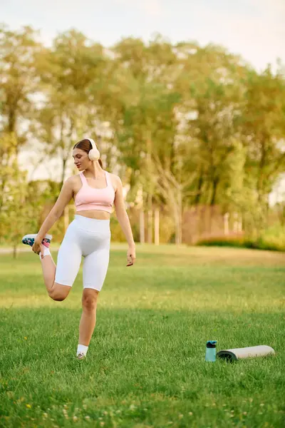 Young athletic woman stretches one leg while preparing for an outdoor workout in a park. — Stock Photo