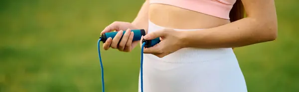 Athletic and beautiful young woman holds jump rope handles with focus under a bright sky. — Stock Photo