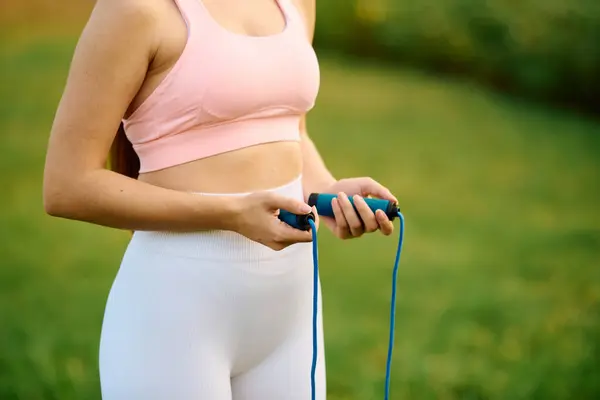 Excited young woman holds a jump rope, ready to start her outdoor fitness routine in the park. — Stock Photo