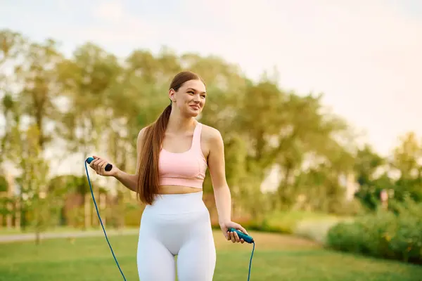 Sporty young woman smiles while jumping rope in a vibrant green park during the day. — Stock Photo