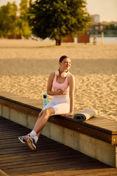 Beautiful woman relaxing on a wooden deck by the beach, wearing sporty clothes and headphones. — Stock Photo